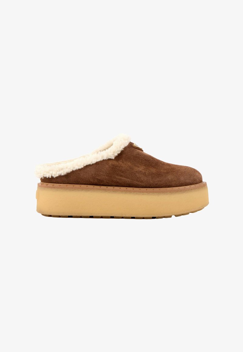 Chaussure mocassin marron en daim avec une épaisse semelle plateforme beige et une doublure blanche duveteuse autour de l'ouverture.