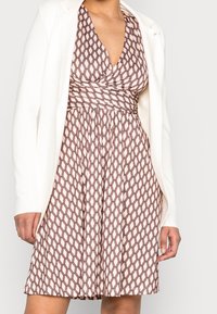 Vestido marrón y crema con estampado, con un escote en V profundo y cintura fruncida, combinado con una blazer blanca. Tejido ligero, hasta la rodilla.