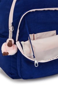 Zaino blu navy con un tessuto testurizzato, dettagli in rosa sulla cerniera e un portachiavi a forma di scimmia in peluche attaccato alla cerniera. Tasca interna visibile.