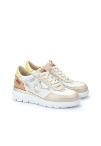 Zapatillas beige y blancas con parte superior perforada, detalles en amarillo claro y suela gruesa. Presentan cordones planos y una etiqueta lateral con la marca.
