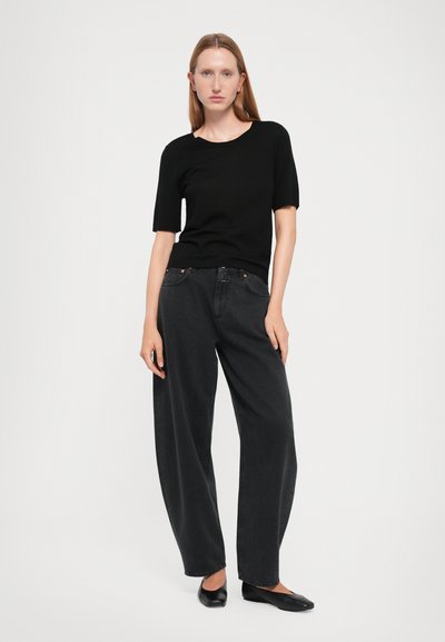 Black short-sleeve top paired with high-waisted, wide-leg black jeans. Material appears textured; shoes are black and pointed. Simple design.