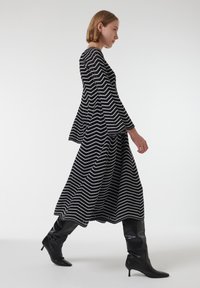 Vestido de patrón zigzag en blanco y negro con mangas largas, silueta acampanada y botas negras de caña alta con punta afilada.