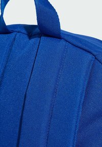 Dettaglio di uno zaino in tessuto blu, caratterizzato da materiale in nylon testurizzato, cuciture rinforzate e cuciture orizzontali sul corpo e sulle maniglie.