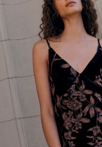 Vestito in velluto nero con scollo a V, caratterizzato da un motivo floreale in rosa tenue. Spalline sottili e vestibilità comoda, con dettagli intricati.
