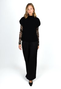 Black textured sweater with puff sleeves over a sheer striped long-sleeve top, paired with wide-leg black trousers and pointed black shoes.