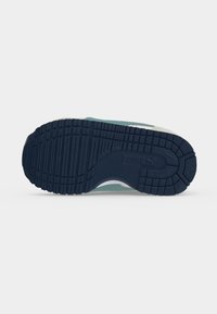 Sole of a sneaker with deep treads and a textured pattern in dark blue rubber, showing grip and traction features.