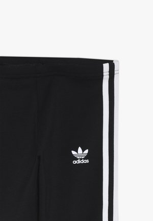 Sección de pantalones negros de Adidas que muestra el logo blanco del trébol y tres rayas blancas a lo largo de la costura lateral sobre un fondo liso.