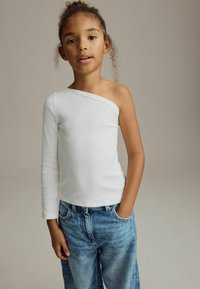 Vit ribbad långärmad topp med den ena axeln bar, kombinerad med ljusblå denimjeans med avslappnad passform och framfickor.