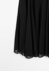 Svart, flödande kjol i lättviktig tyg, med en genomskinlig textur och lagerdesign som har en fåll som faller mjukt.
