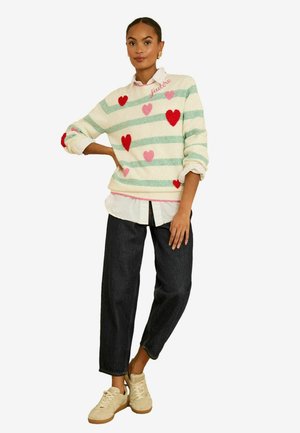 Megztinis su žaliomis ir baltomis juostelėmis, raudonomis ir rožinėmis širdelių raštais bei rožine siuvinėjimo užrašu „j'adore“. Derinamas su tamsiais džinsais ir sportbačiais.