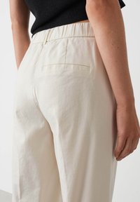 Crème-kleurige, loszittende broeken met een elastische tailleband en een enkele achterzak, gemaakt van een gladde, lichte stof.