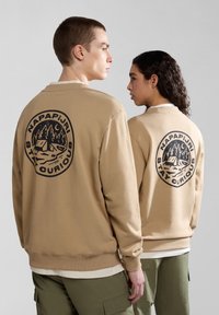 Felpa beige con un grande grafico circolare nero sul retro che raffigura montagne, alberi e la scritta "NAPAPIJRI STAY CURIOUS", con polsini a costine.