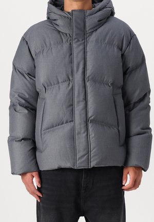 Osoba ubrana w szarą, pikowaną zimową kurtkę z wysokim kołnierzem, zamkiem błyskawicznym i bocznymi kieszeniami, w połączeniu z czarnymi spodniami.