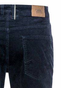Navy corduroy broek met een patchlabel, voorzien van een rechter achterzak en een subtiele textuur. De achterkant benadrukt de naaddetails.