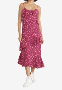 Fuchsia Kleid mit Spaghettiträgern, Rüschensaum und -hals, florales Muster, gestuftes Design, kombiniert mit weißen Sneakers.