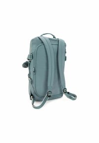 Sac à dos vertical rectangulaire bleu avec des bretelles rembourrées et ajustables, plusieurs compartiments zippés et un petit charme en pompon attaché sur le côté.