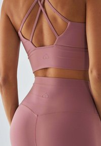 Jasnoróżowy sportowy biustonosz z krzyżującymi się ramiączkami, w zestawie z legginsami z wysokim stanem, ozdobionymi małym logo serca na pasie.