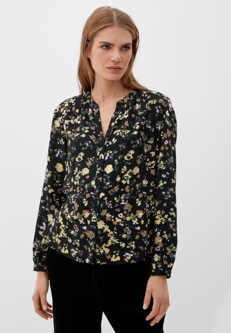Schwarze Bluse mit Blumenmuster, mit durchgehender Knopfleiste, langen Ärmel und lockerer Passform. Der Stoff hat eine weiche Textur mit mehrfarbigen Blumenmustern.