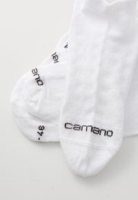 Bijele anklet čarape izrađene od teksturirane tkanine, s crnim 'camano' logotipom i dodatnim printanim detaljima u blizini područja prstiju.
