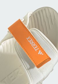 Ελαφριά λευκά αθλητικά σανδάλια με πορτοκαλί ρυθμιζόμενο λουράκι; επάνω μέρος από δίχτυ, υφή στη σόλα και εμφανές λογότυπο "TERREX".