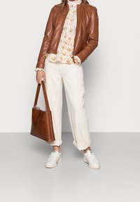 Hnědá kožená bunda, květinová blůza, bílé kalhoty, hnědá kabelka a bílé tenisky. Blůza má krajkové detaily a volnější střih.