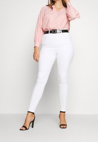 Różowa i biała bluzka w paski z dekoltem w serek, z bufiastymi rękawami. Białe skinny jeans, czarny pasek z srebrnym okuciem. Czarne sandały na obcasie.