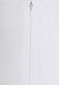 Valkoinen pellavavaate, jossa metallinen vetoketjusuljin ja saumat, korostaen sileää, teksturoitua pintaa.