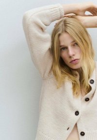 Cardigan de punto en beige claro con escote en V profundo, que presenta botones marrón oscuro, puños acanalados y un acabado texturizado.