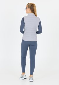 Ljust grå pufferväst, stretchiga navy långärmade tröjor, navy leggings och silverfärgade träningsskor. Släta texturer med färgkontrast. Ingen synlig logotyp.