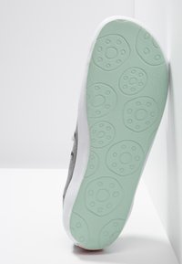 Semelle de baskets grises avec une semelle intermédiaire blanche, semelle extérieure en caoutchouc vert clair présentant des motifs circulaires et une texture antidérapante.