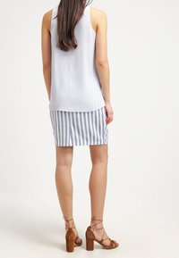 Světle modrý top bez rukávů spárovaný s bílou a světle modrou pruhovanou sukní. Modelka má na sobě hnědé sandály na podpatku s pásky kolem kotníků.