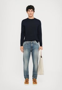 Navy long-sleeve shirt, light blue jeans, brown sneakers, and a beige tote bag. Simple design with a relaxed fit and minimal detailing.