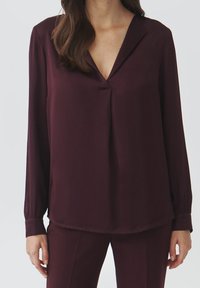 Burgunderfarbene Bluse mit langen Ärmeln aus glattem Material, mit einem V-Ausschnitt, lässiger Passform und sanfter Drapierung an der Vorderseite.