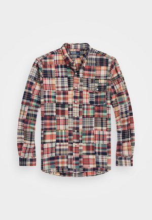 Camisa de cuadros de algodón con una mezcla de patrones en rojo, verde, azul marino y crema, con cuello abotonado y un solo bolsillo en el pecho con detalle de botón.