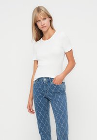 Witte, korte mouwen, slim-fit top in ribbelstructuur, gecombineerd met blauwe denim jeans met een ruitpatroon en zilverkleurige accenten.