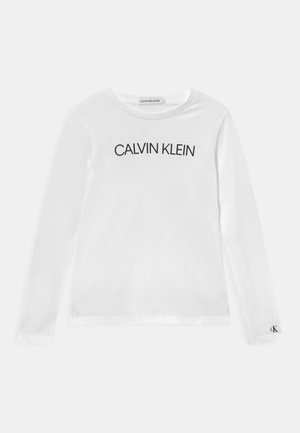 Chemise blanche à manches longues avec texte noir "CALVIN KLEIN" centré sur la poitrine et petit logo "cK" sur le poignet de la manche gauche.