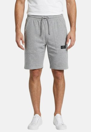 Homme portant un short gris clair à cordon de serrage avec poches plaquées et des baskets blanches, debout les bras détendus le long du corps.