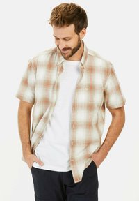 Kurzärmliges, karierte Hemd in Beige und Hellrot, aus leichtem Stoff. Mit Button-Down-Kragen und Brusttasche, über einem weißen T-Shirt getragen.
