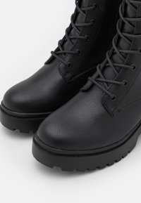 Bottes noires à lacets en cuir texturé avec un bout arrondi et une semelle épaisse et robuste, dotées d'œillets en métal et de lacets plats.