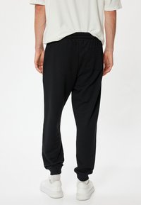 Sorte sweatpants med en tætsiddende design, elastisk talje og en baglomme, parret med hvide sneakers og en løs, lyset-shirt.