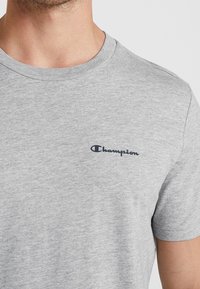Szara koszulka z bawełnianej mieszanki, z okrągłym dekoltem i małym granatowym logo Champion na lewej piersi. Miękka w dotyku i o luźnym kroju.