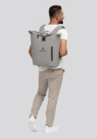 Zaino impermeabile grigio con chiusura a rotolo, spallacci regolabili e tasca laterale con zip. Logo stampato sulla parte anteriore. Materiale liscio e resistente.