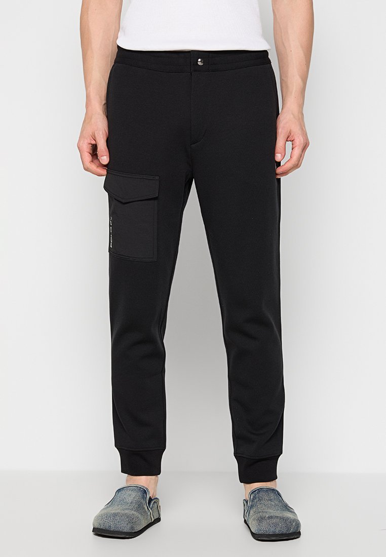 Czarne dresy o zwężanym kroju, z boczną kieszenią cargo, elastycznym pasem i ściągaczami, wykonane z miękkiego materiału.