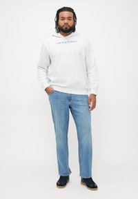 Lys grå hettegenser med logo foran, bomullsblanding; kombinert med blå denimjeans, rette ben, brukt med mørke joggesko, minimalistisk design.