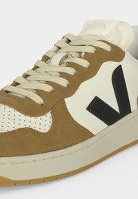 Παπούτσι τύπου low-top με μπεζ επενδύσεις από καστόρι, μπεζ δερμάτινη μύτη με τρύπες, μαύρο λογότυπο "V" και μπεζ κορδόνια σε λευκή σόλα με καουτσούκ εξωτερική σόλα.