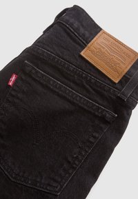 Black denim jeans with a back pocket featuring a stitched heart design. Tan leather patch with brand logo and details on the waistband.