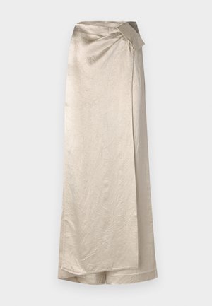 Długa, beżowa spódnica wykonana z błyszczącego, teksturowanego materiału. Posiada fason na zawijanie z boczną kokardą i schludnym dołem.