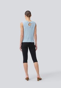 Lyseblå heklet tank topp med nøkkelhullsdetalj på ryggen, parret med sorte hverdags leggings. Jevn tekstur og bølgete kant.