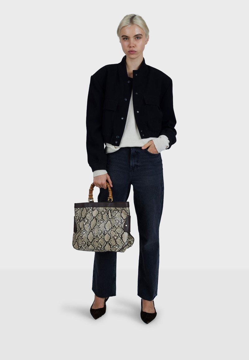 Sort cropped jakke over en hvid top, kombineret med mørke jeans og sorte hæle. Holder en beige håndtaske med slangeskindsmønster og bambushåndtag.