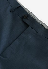 Dark blue dress pants waistband with black button closure, belt loop, and visible front pocket on a white background.